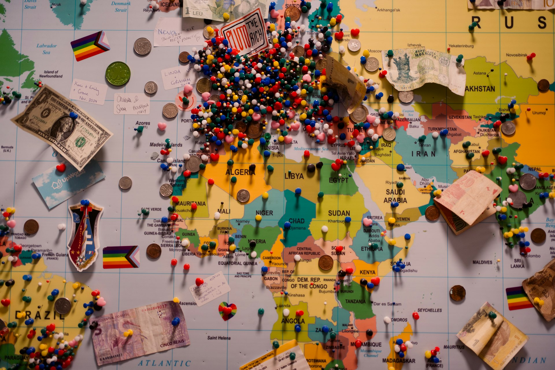 A world map is covered with pins and mementos.